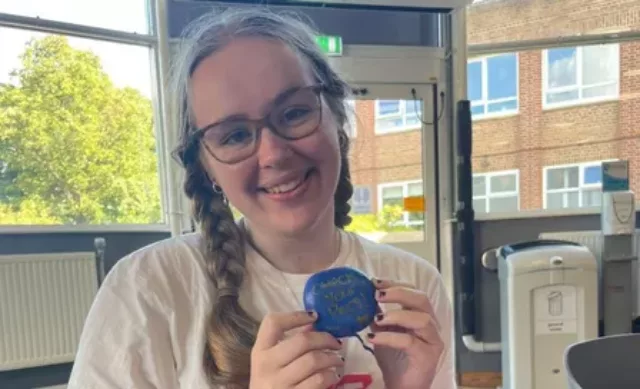 a woman from one of our university boob teams holding a rock that she has painted whihc reads 'check your boobs'