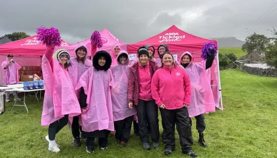 A group of Tickled Pink fundraisers wearing rain macs in front of a CoppaFeel! gazebo.